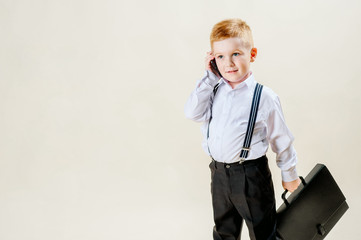 little red-haired boy in a business suit with a phone in his hand hurries to a meeting in a business suit, business, mini boss