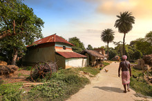 Rural Man Walking Along An Unpaved Village Road With View Of Mud Houses At Sunset. Photograph Shot At Bolpur, West Bengal India