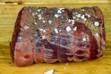 Rolled beef brisket on a wooden chopping board seasoned with sea salt flakes and pepper.