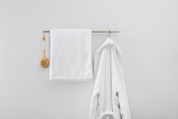 Rack with clean bathrobe, brush and towel on light wall