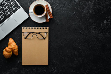 Laptop, coffee and croissant. Breakfast. On a black stone background. Top view. Free space for your text.