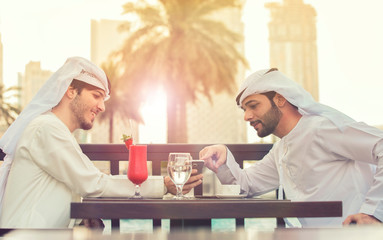 Wall Mural - two Arab man talking . they sits at a table in a cafe, and drink red juice at Dubai in evening