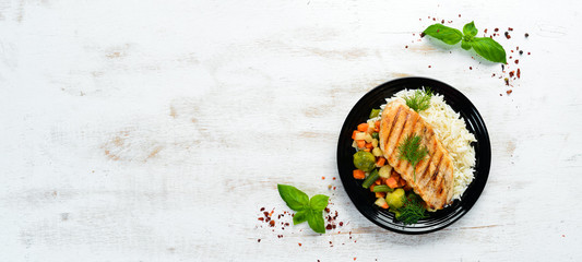 Wall Mural - Baked chicken fillet with rice and vegetables on a black plate. Top view. Free copy space.