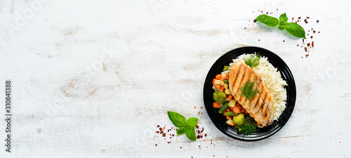 Baked chicken fillet with rice and vegetables on a black plate. Top view. Free copy space.