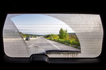 dirty car view from inside the car through the rear window, rear window of a dirty car with a view of the asphalt road with markings and road traffic.