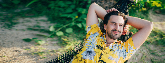 Wall Mural - A young man lies in a hammock on a sunny beach.