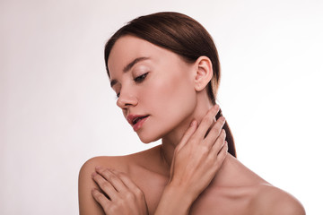 Side view of young brunette woman with healthy glowing face skin. Posing naked on camera. Hold hands on neck and shoulder. Face treatment and skincare. Isolated over light background.