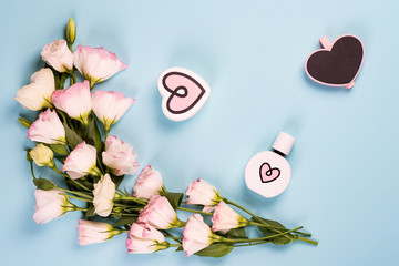 Wall Mural - Blooming pink eustoma with parfume heart and wooden chalk board, flat lay. Floral decorative corners on blue background.