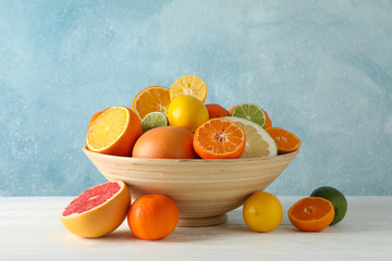 Juicy citrus fruits in bowl on wooden table against blue background, space for text