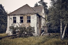 Old Abandoned House On A Grassy Field Surrounded By Trees