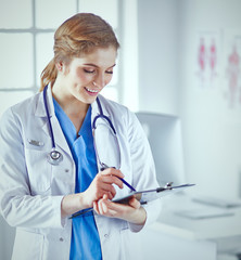 Wall Mural - Young woman doctor is standing with board with clipboard smilin