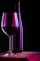 Glass of red wine with bottle on wooden table and dark background