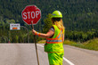 A close up and rear view of a female road construction worker holding a stop stick wearing high visibility safety clothes, roadworks traffic control