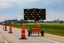 A Close Up Shot Of An LED Mobile Matrix Keep Left Sign, With Orange Flashing Lights Warning Motorists With Arrows And Road Cones During Lane Closure