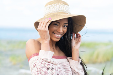 Pretty African American woman wearing floppy hat with a smile at the beach