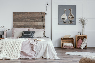 Spacious, feminine bedroom interior with rustic furniture, white walls, wooden crates and oil painting of animals. Real photo