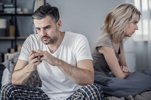 Man In Pajamas Sitting In Bed And Taking Off His Wedding Ring After Argument With His Wife