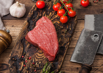 Slice of Raw Beef sirlion steak on wooden chopping board with tomatoes,garlic and asparagus tips and meat hatchets.