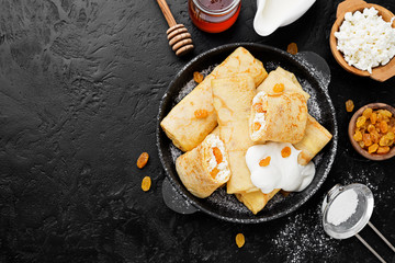 Wall Mural - Thin pancakes or crepes stuffed with cottage cheese and raisins on black background. top view