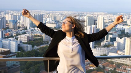 Young Businesswoman With Arms Raised On Skyscraper Top In City
