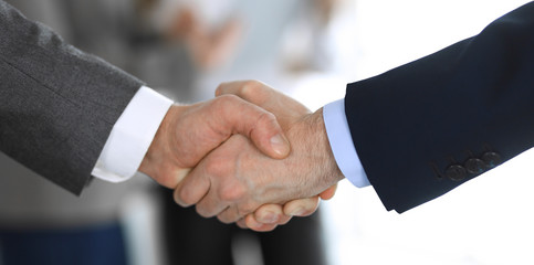 Business people shaking hands while standing with colleagues after meeting or negotiation, close-up. Group of unknown businessmen and women in modern office. Teamwork, partnership and handshake