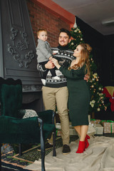 Wall Mural - Beautiful family sitting near Christmas tree. Cute mother in a green dress. Little boy with handsome father