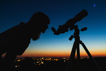 Wall Mural - astronomer with a telescope watching at the stars and moon with blurred city lights in the backgroun