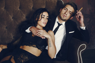 Elegant man in a black suit. Couple at home. Hot woman in a black underwear. Male with cigar