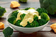 Broccoli With Cheese Sauce In White Bowl On Wooden Table