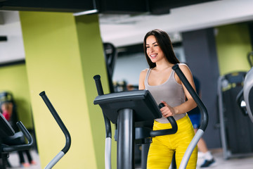 Wall Mural - Young fitnes girl exercising on cross trainer machine