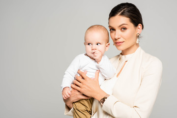 beautiful smiling businesswoman holding baby boy on hands, isolated on grey