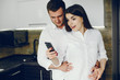© hetmanstock2 - Cute couple on a kitchen. Pretty brunette in a white shirt. Man and woman use the phone