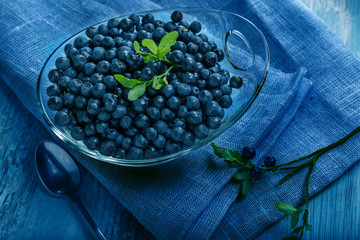 Wall Mural - Freshly blueberries in glass bowl. Juicy and fresh blueberries with green leaves on blue wooden table. Concept for healthy eating and nutrition.