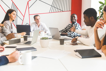 Wall Mural - A team of young office workers, businessmen with laptop working at the table, communicating together in an office. Corporate businessteam and manager in a meeting. coworking.