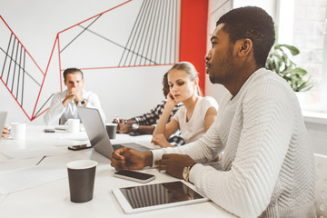 Wall Mural - A team of young office workers, businessmen with laptop working at the table, communicating together in an office. Corporate businessteam and manager in a meeting. coworking.