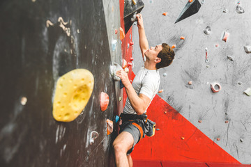 Wall Mural - Sportsman climber moving up on steep rock, climbing on artificial wall indoors. Extreme sports and bouldering concept