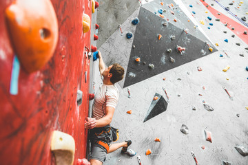 Wall Mural - Sportsman climber moving up on steep rock, climbing on artificial wall indoors. Extreme sports and bouldering concept