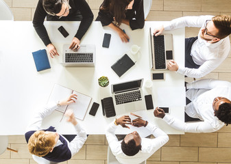 A team of young businessmen sitting at the table, top view, working and communicating together in an office. Corporate businessteam and manager in a meeting.