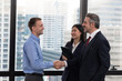© Sathaporn - Senior executive shaking hands with young employee with secretary holding clip board in the office with building background