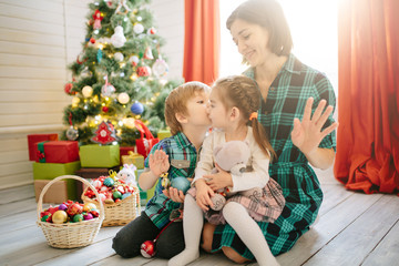 Wall Mural - Happy family mom, son and daughter on a Christmas winter sunny morning in a decorated Christmas celebration room with a Xmas tree and gifts.