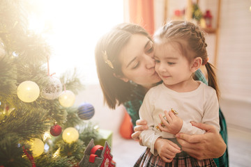 Wall Mural - Happy family mom and daughter on a Christmas winter sunny morning in a decorated Christmas celebration room with a Xmas tree and gifts.