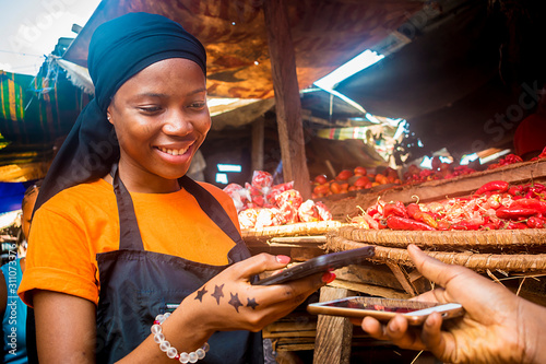 Fotografía young african woman selling tomatoes in a local african market receiving payment