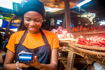 Wall Mural - young african woman selling tomatoes in a local african market using her mobile pos device