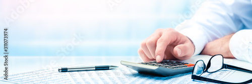Cuadros en Lienzo Business Man Using Calculator On Desk With Pen, Reading Glasses, And Financial R