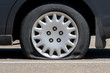 © madscinbca - Flat tire on an unidentifiable black car. Low angle closeup view. No markings or identification on the car or tire.