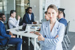 © xartproduction - Business woman stands on the background of partners. A team of young businessmen working and communicating together in an office. Corporate businessteam and manager in a meeting