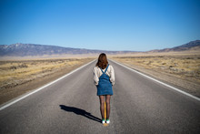 A Young Woman In Vintage Clothes Stands In The Middle Of The Road In Nowhere