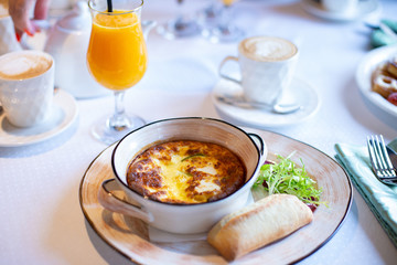 Breakfast Italian omelet baked with cheese on a plate with bread and green salad on a table with a glass of orange juice.