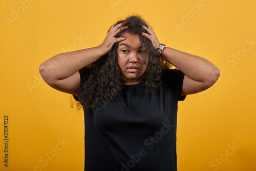 Cuadros en Lienzo Crazy afro-american young woman with overweight over isolated orange background wearing fashion black shirt keeping hands on head, corrects haircut