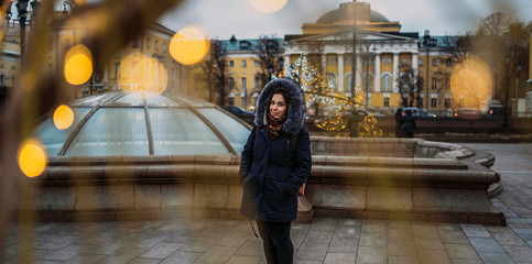 Portrait of a beautiful young woman in a jacket and hood through a garland on the street.